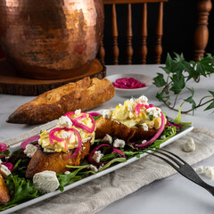 Creamy egg salad tops grilled slices of baguette on a bed of arugula. Garnished with pickled red onions and crumbled goat cheese.