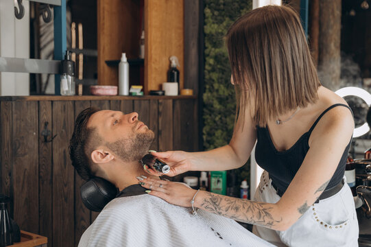 Tattooed barber trimming beard of client