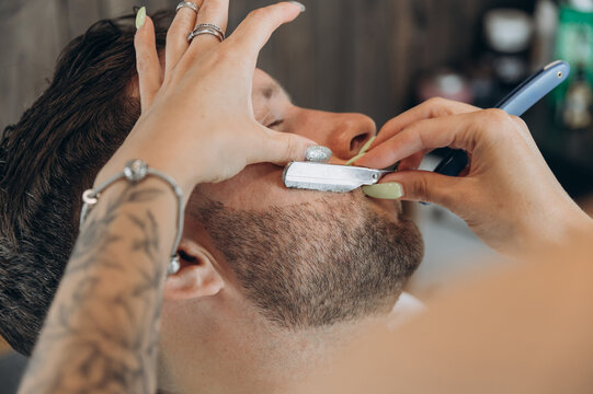 Crop barber shaving beard with razor