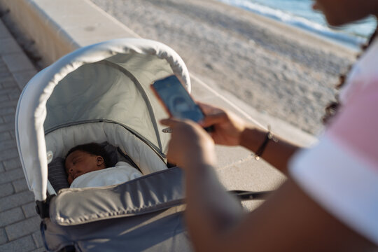 Crop black woman photographing sleeping baby near beach