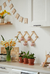 Bouquets of daffodils on a light table. In the background, the interior of a white Scandinavian-style kitchen. The concept of home comfort. Holiday concept.