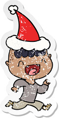 distressed sticker cartoon of a happy boy laughing and running away wearing santa hat