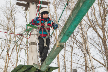 A cute little boy in a hard hat climbs in an adventure park, passing an obstacle course. high rope park