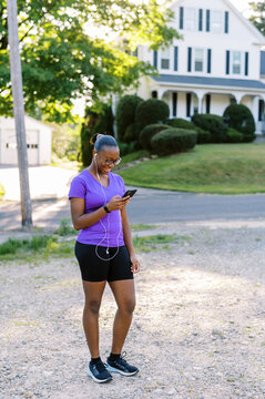 Young black teen in active wear holding phone, wearing headphones