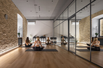 Girls doing yoga training inside hall with mirrored wall
