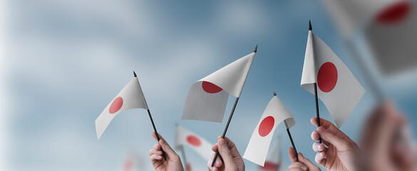 Fototapeta na wymiar A group of people holding small flags of the Japan in their hands