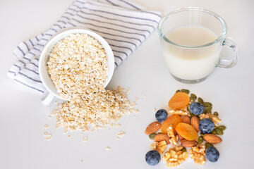 Healthy breakfast concept. Dry rolled oatmeal in bowl, dried and fresh fruit, cup of milk, isolated on white background