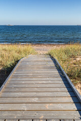 Fototapeta premium Wooden boardwalk leading to an empty beach in Hanko, Finland, on a sunny day in the summer.