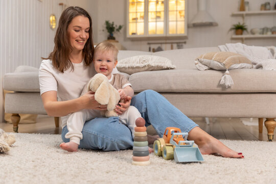 Happy family at home. Mother and baby boy playing with toys at home indoors. Little toddler child and babysitter nanny having fun together. Young woman mom kid son rest in living room