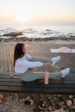 shot of a woman tying her shoes while sitting on a bench near the sea