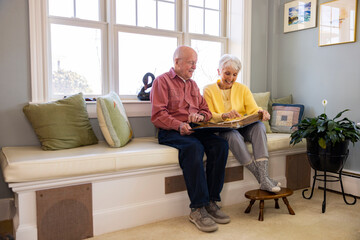  Senior Citizen couple in living room laugh at family photo album 