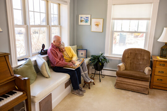 Casual Senior Citizen couple at home hug at family photo album 