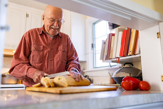  Senior Citizen man at home cutting bread with knife alone