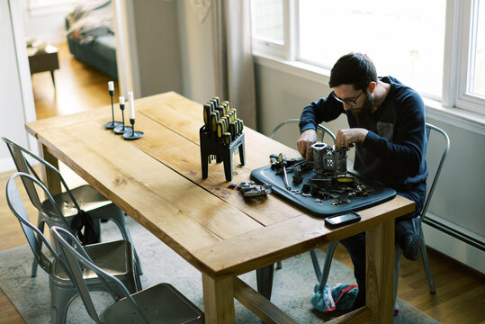Millennial Man assembling carburetor on kitchen table in his home 
