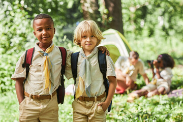 Waist up portrait of two boy scouts looking at camera while camping with school group, copy space - obrazy, fototapety, plakaty