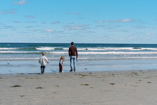 Millennial father walking on New England beach with his children