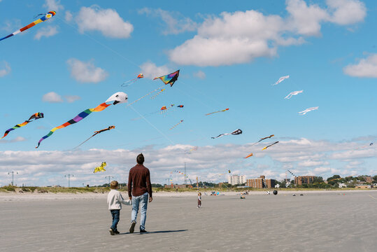 Young family walking on massachusetts beach under flying kites
