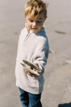 Little boy holding seashell in his hands on New England beach