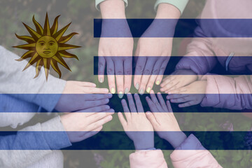 Fototapeta na wymiar Hands of kids on background of Uruguay flag. Uruguayan patriotism and unity concept.