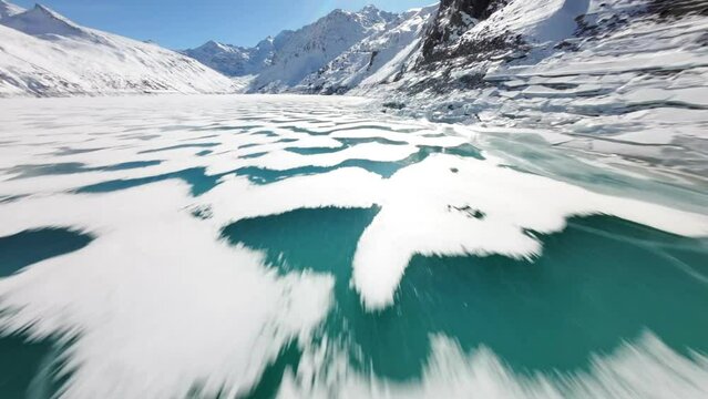 Breathtaking FPV drone flight over the frozen surface of the Mattmark Dam reservoir in Switzerland, revealing stunning contrasts between turquoise ice, white snow, and the majestic alpine mountains