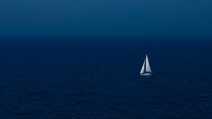 Fototapeta premium White boat swimming in a dark blue sea in the evening with sky background