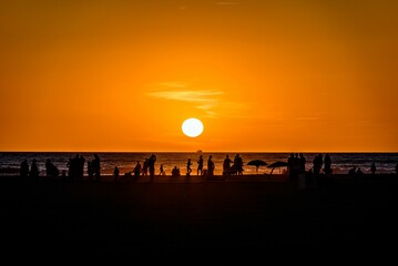 Silhouette of a beach full of people under the cloudless red sunset sky reflected on the sea
