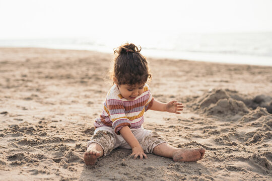 Toddler Girl Sitting and Playing At The Beach

