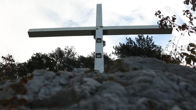 Undershot of wooden cross on the mountains, trees against cloudy sky
