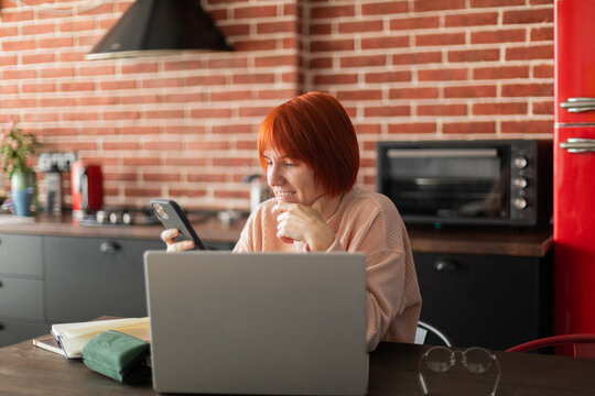 Woman working on the kitchen with phone and laptop