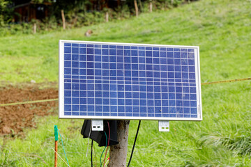 small solar system to power a livestock fence in front of a green meadow. a day without people