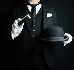 Portrait of Butler in Dark Formal Suit and White Gloves Brushing a Bowler Hat. Concept of Service Industry and Professional Hospitality.