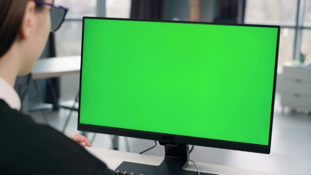 Young Girl Working At Computer With Green Mock Up Screen in Office. Close Up Desktop Computer Monitor with Mock Up Green Screen Chroma Key Display
