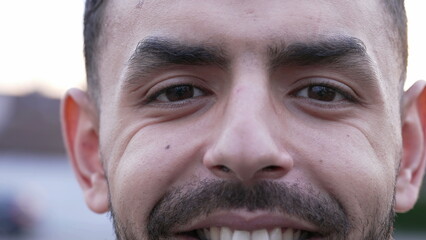 Obraz premium One Middle Eastern young man close up face and eyes smiling at camera. An Arab 20s male person with wrinkles