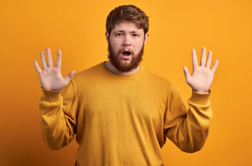 Body language concept. Frightened man with fearful expression, gestures with palms, makes defense sign, exlaims with astonished expression, dressed in red casual t shirt isolated.