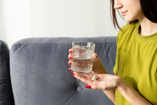 Woman holding supplements and glass of water in hands 