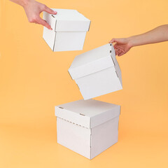 Hands hold white craft boxes of different sizes on an orange background. Place for text and logo. The concept of packaging, padarunka, moving. High quality photo