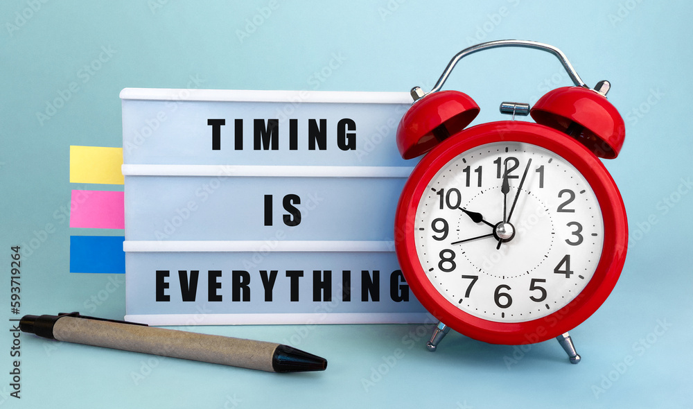 Poster text timing is everything written on the lightbox with alarm clock and colorfull stickers on blue ba