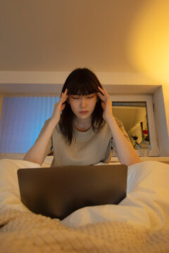 Tired Asian woman using laptop in bedroom