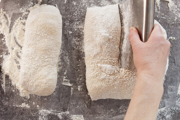 A woman's hand cuts the dough into pieces with a knife. Cooking bread, ciabatta.