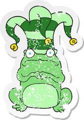 retro distressed sticker of a cartoon nervous frog wearing jester hat