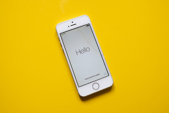 A White IPhone 5s With A Cracked Screen Against A Clean Yellow Background