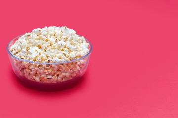 Popcorn in a large glass bowl on a pink background. Crispy classic popcorn snack for watching movies and series. Delicious snack for spending free time and watching TV. Free space for text