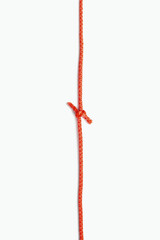 The two ends of a red rope are tied in a knot on a white vertical background. Red nylon rope with a...