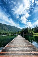 Idyllic view of a wooden pier in the lake with lush forested mountain in the background under wispy clouds