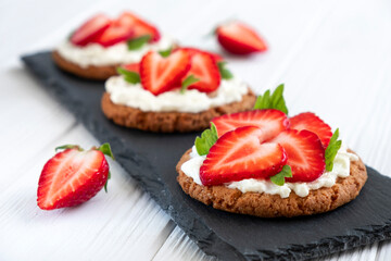 Healthy crispbread bruschetta with strawberry and cream cheese on slate board. Healthy snack, clean eating or dieting concept. Recipe of vegan food for everyday cooking.