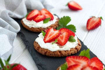 Fototapeta na wymiar Healthy toast with strawberry, cream cheese and mint leaf. Tasty breakfast. Clean eating, dieting or recipe of healthy snack sandwich for vegetarian. Restaurant serving on slate board.