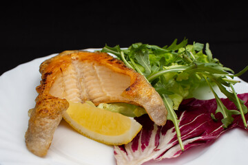 On a plate a delicious piece of fish with lemon and salad