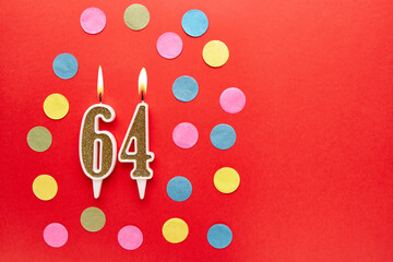 Number 64 on a red background with colored confetti. Happy birthday candles. The concept of...