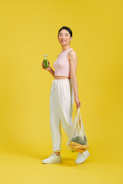 Happy woman with green juice holding string bag with fruits