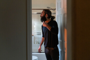 Man trims beard through doorway of bathroom